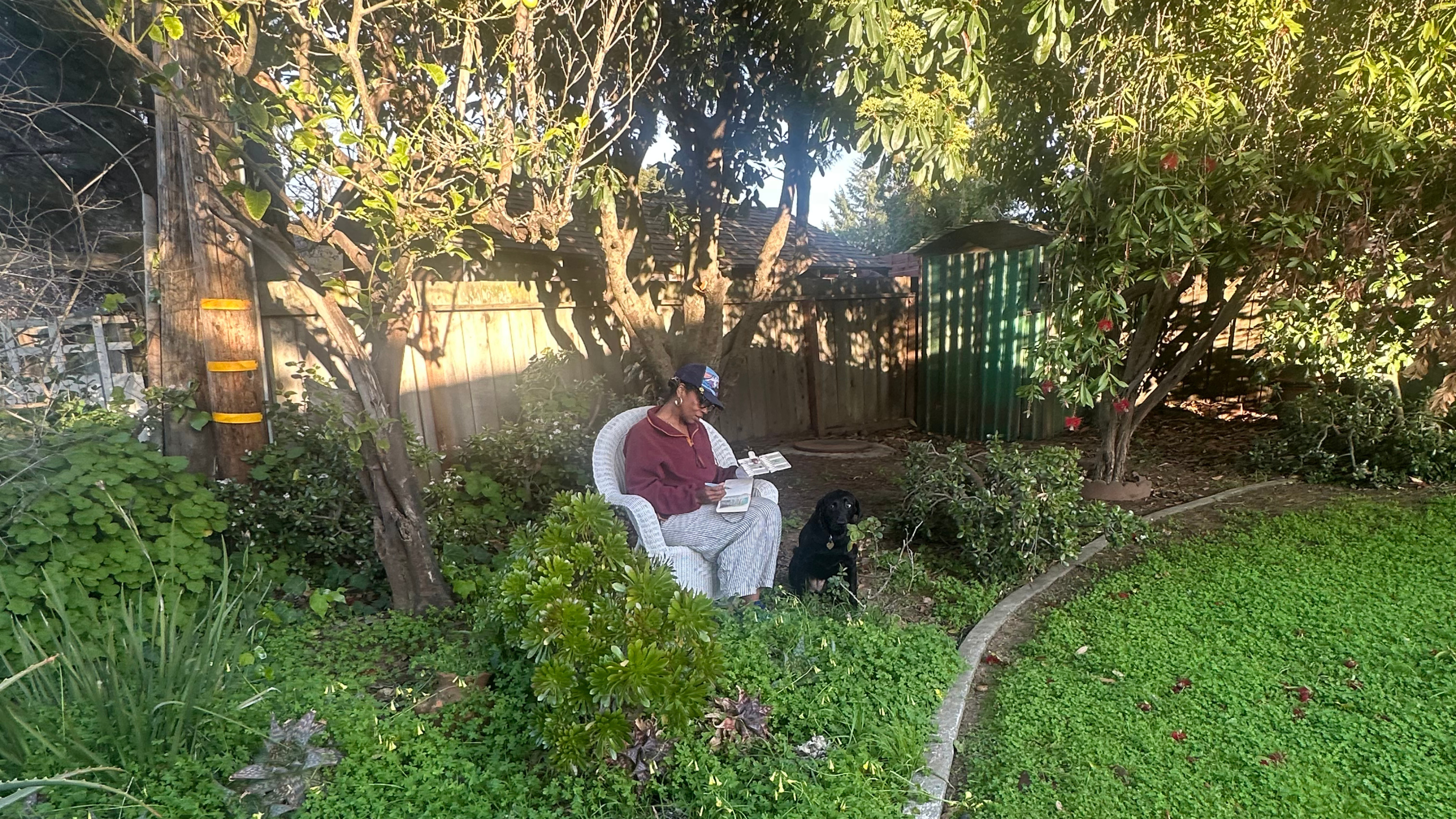 Rue Mapp sitting in a white wicker chair in a lush, green backyard garden